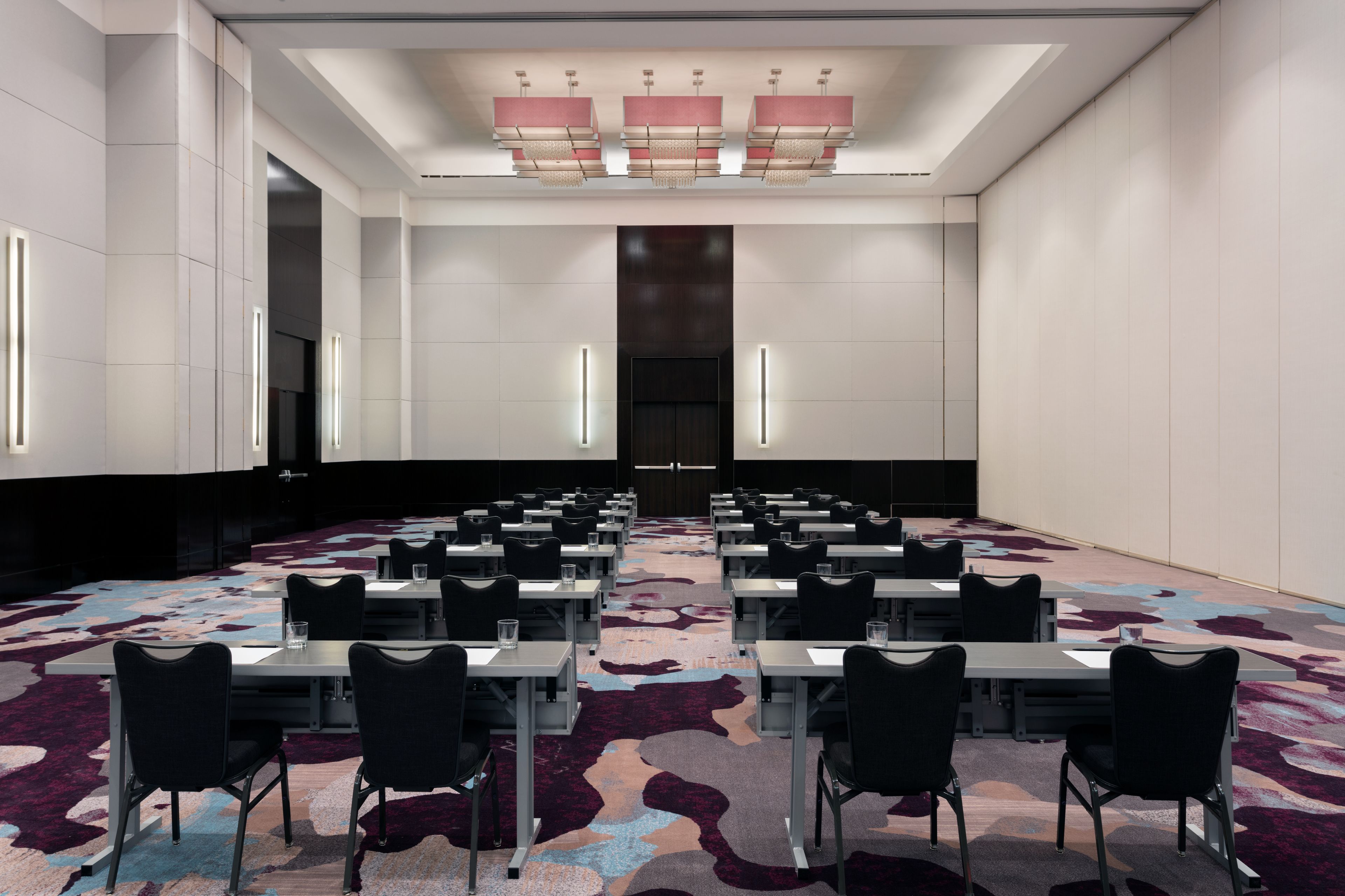 Une salle de conférence avec des rangées de tables et de chaises, une moquette à motifs et un lustre moderne.