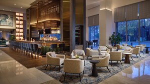 A spacious lobby with a bar area, comfortable seating, and large windows offering views of the outdoors. - Loews Atlanta Hotel (Atlanta)