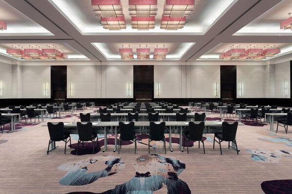 A large conference room with multiple tables and chairs, high ceilings with skylights, and a patterned carpet.