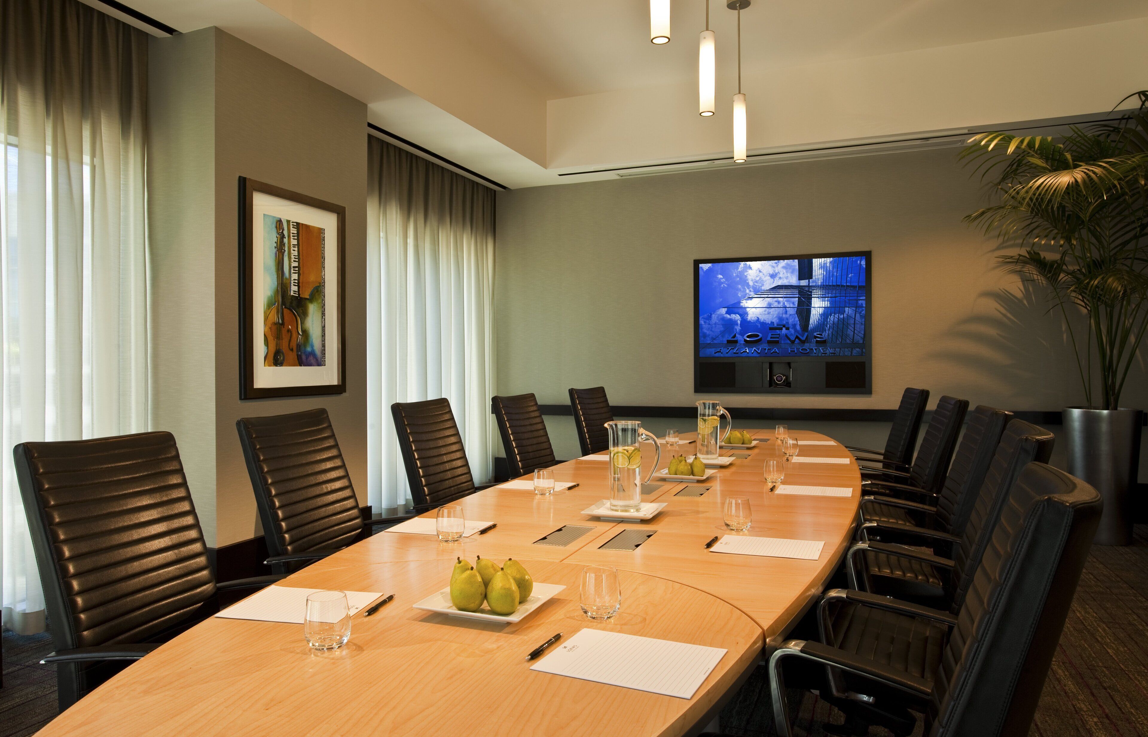 A conference room with a long table, chairs, a TV screen, and a framed artwork on the wall.