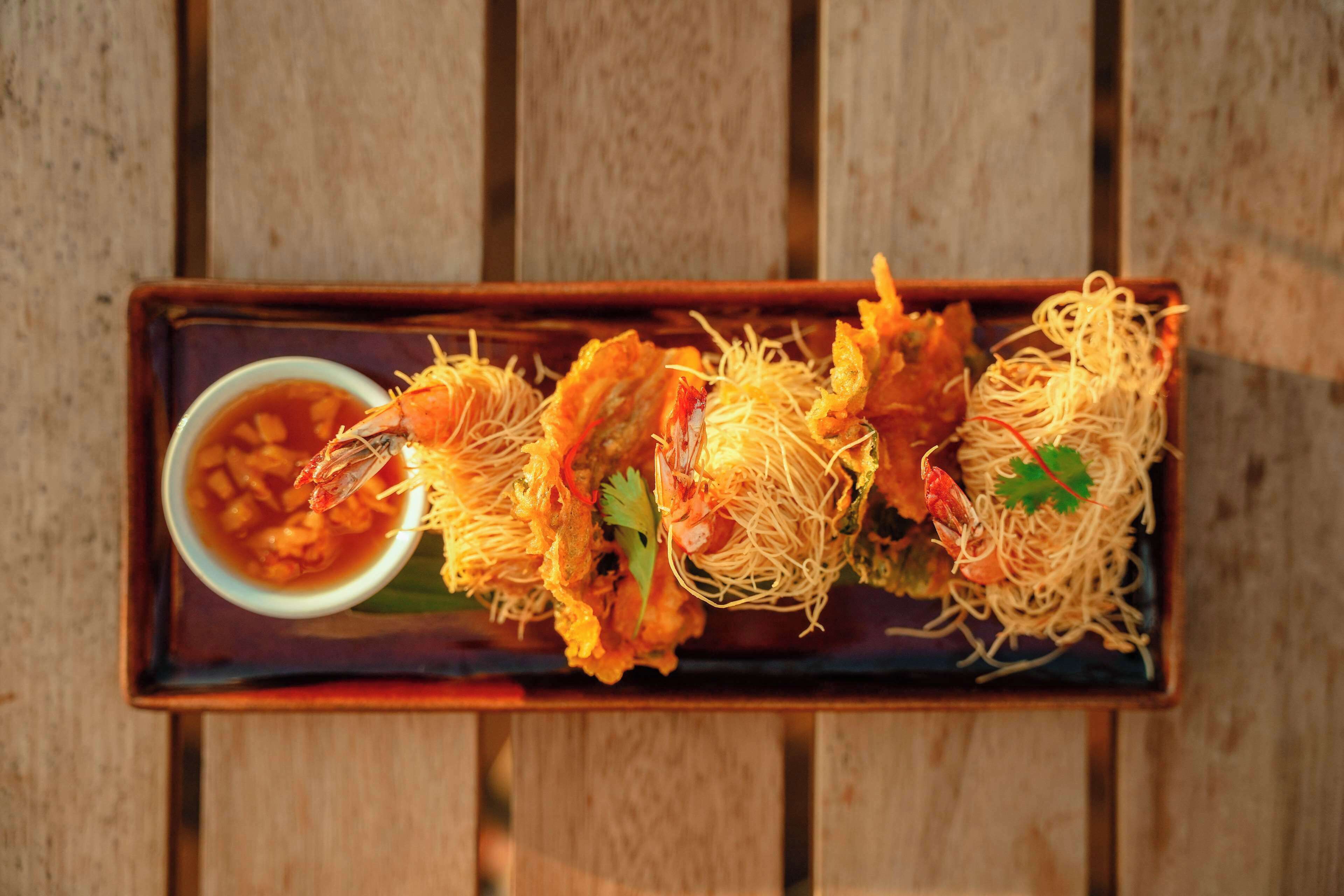 A rectangular tray with a dish of fried seafood and noodles, accompanied by a small bowl of sauce.