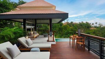 Une terrasse en bois avec des chaises longues et une table, donnant sur une piscine et une végétation luxuriante.