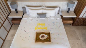 Una cama bien hecha con un cartel de 'Happy Birthday', un postre en una bandeja y dos lámparas sobre mesitas de noche.