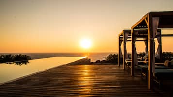 Relax by the infinity pool overlooking the ocean, surrounded by a wooden deck and shaded seating area.