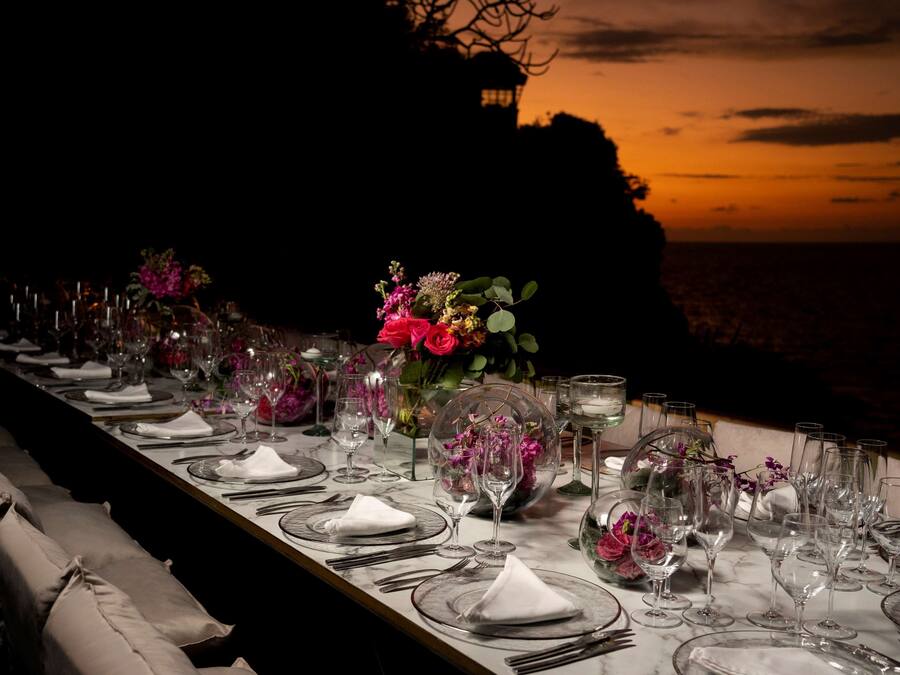 A long dining table set for a formal meal with multiple place settings, glasses, and floral centerpieces.