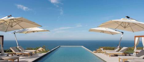 A poolside area with lounge chairs and umbrellas, overlooking a clear blue sky and the ocean.