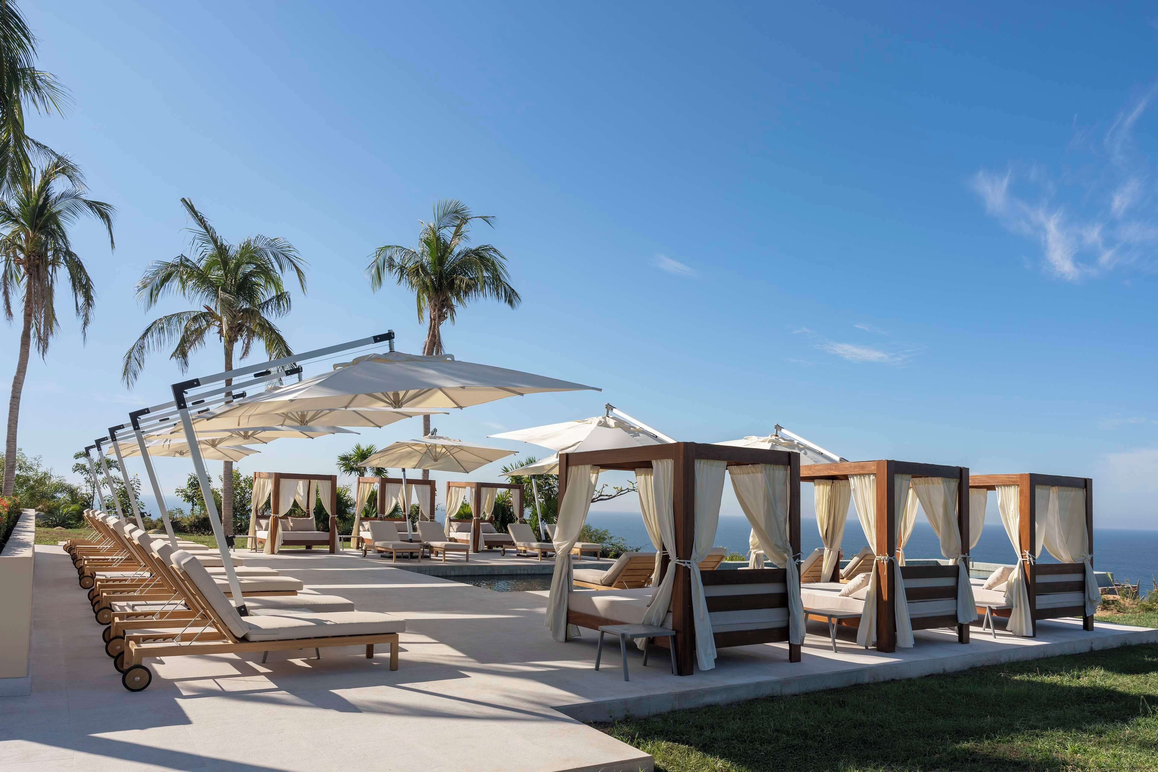 A resort with outdoor seating areas, including lounge chairs and a poolside cabana, overlooking the ocean.