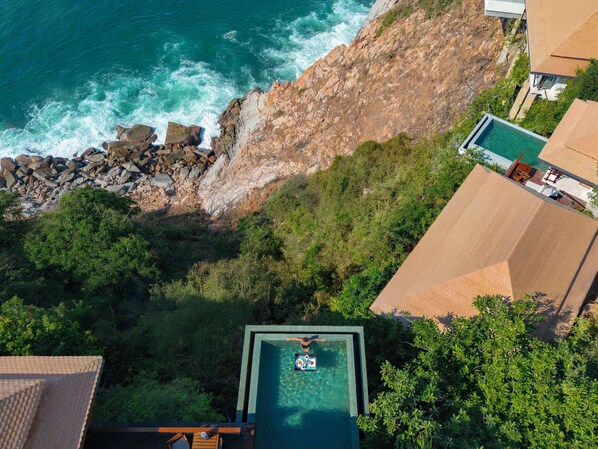 An infinity pool with a clear view of the ocean, surrounded by lush greenery and rocky terrain. - Banyan Tree Cabo Marques (Acapulco)