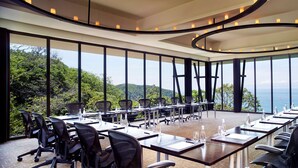 Una sala de conferencias con vistas panorámicas al mar y las colinas, amueblada con mobiliario moderno y una lámpara circular en el techo.