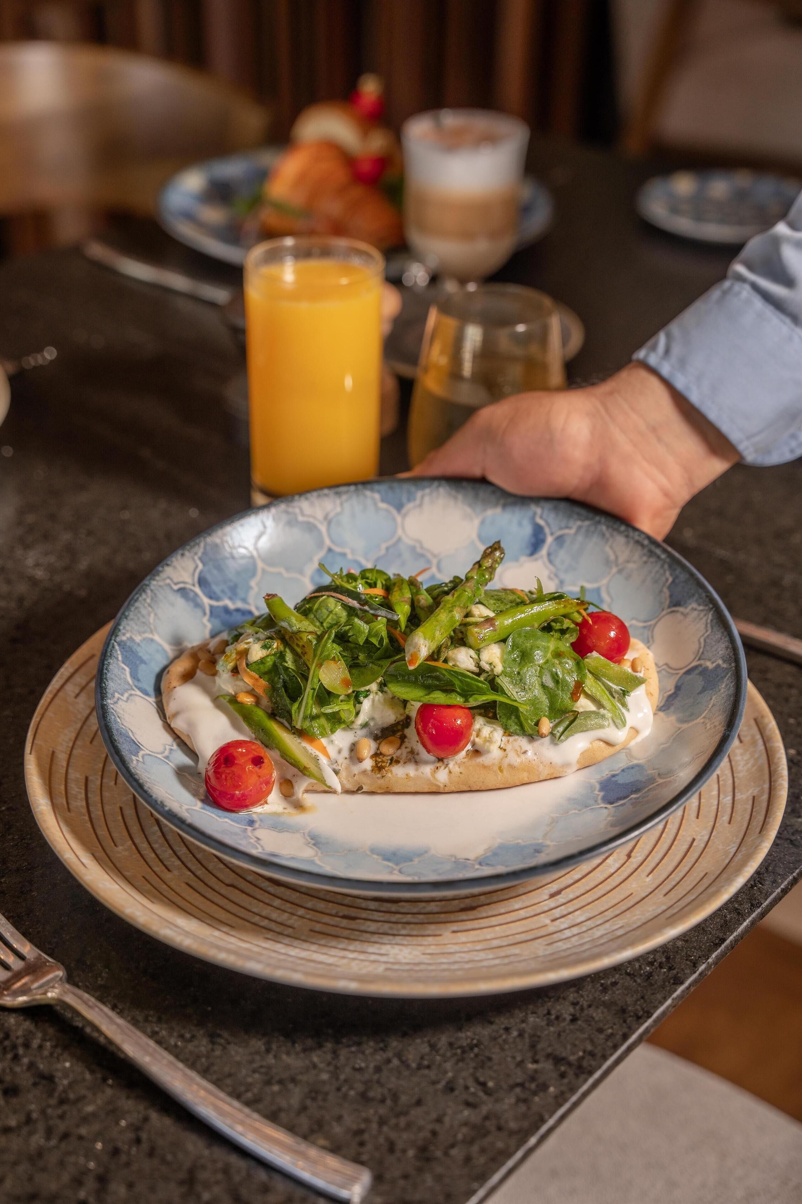 A plate of food on a table with a glass of orange juice and a cup of coffee in the background.