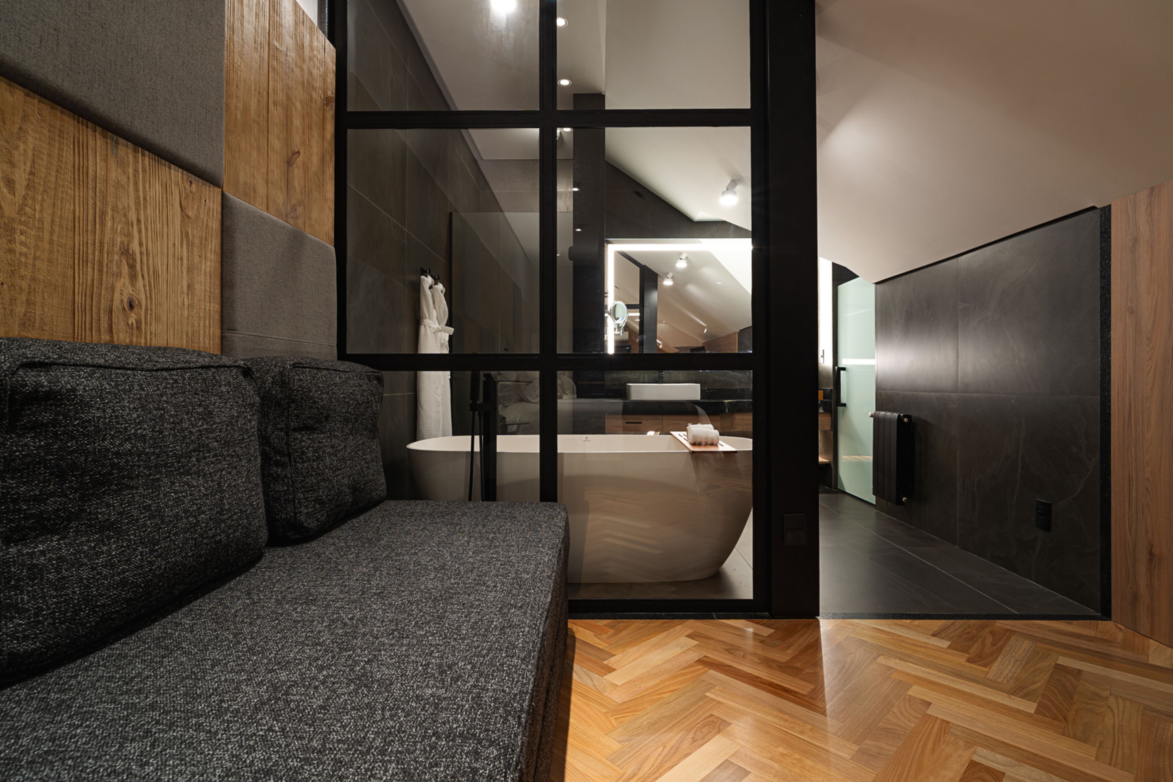 A modern bathroom with a large bathtub, a wooden floor, and a gray sofa.