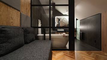A modern bathroom with a large bathtub, a wooden floor, and a gray sofa.