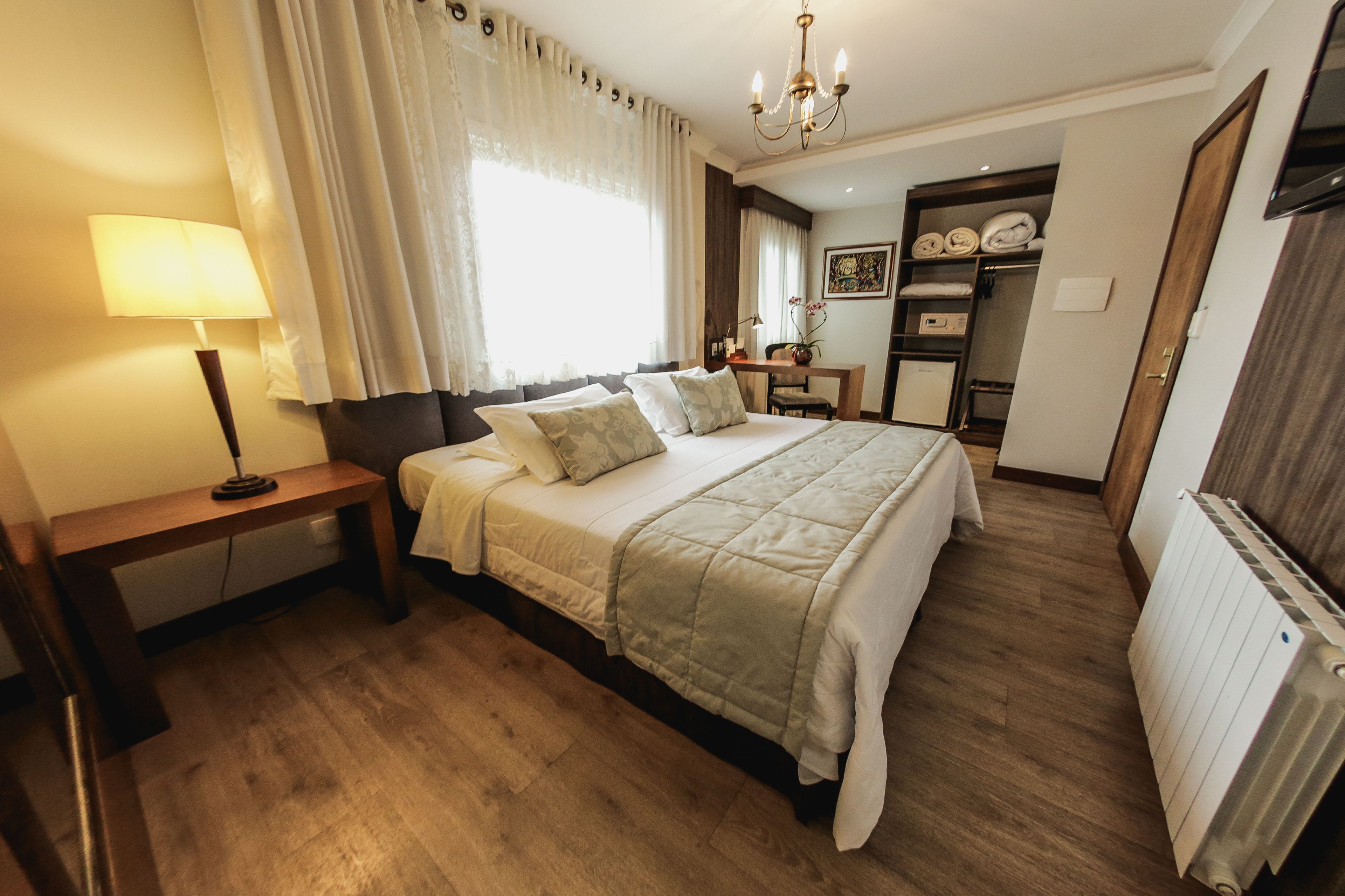 A bedroom with a bed, bedside table, lamp, and a view of a bathroom with a shower and toilet.