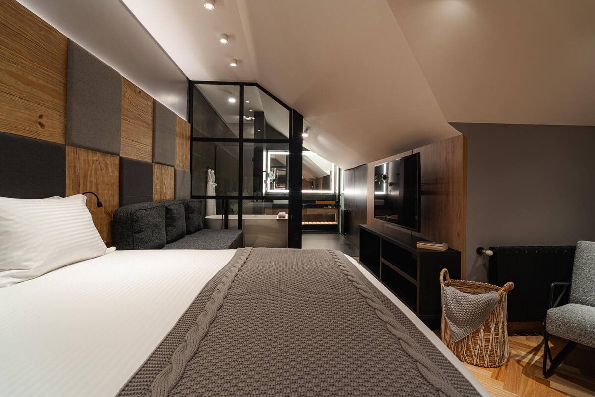 A modern hotel room with a large bed, a seating area, a television, and a small side table.