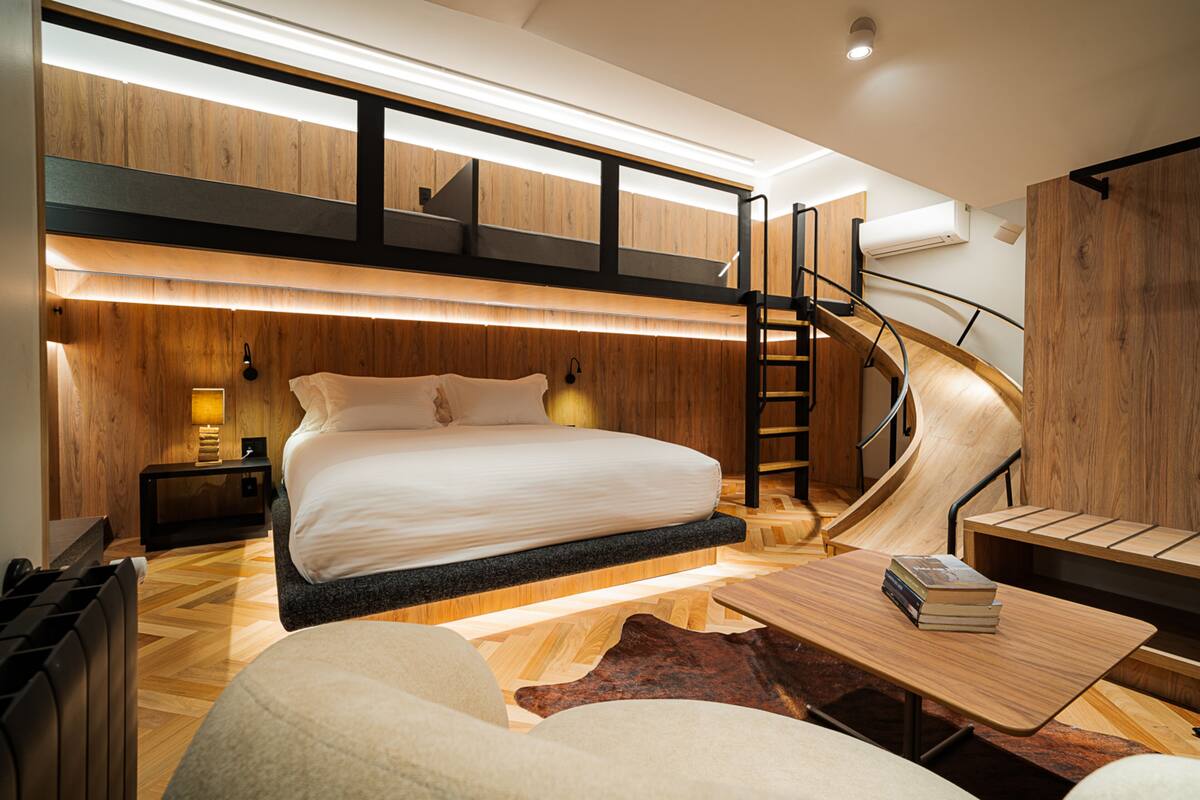 A modern bedroom with a bunk bed, a wooden desk, a spiral staircase, and a large window.
