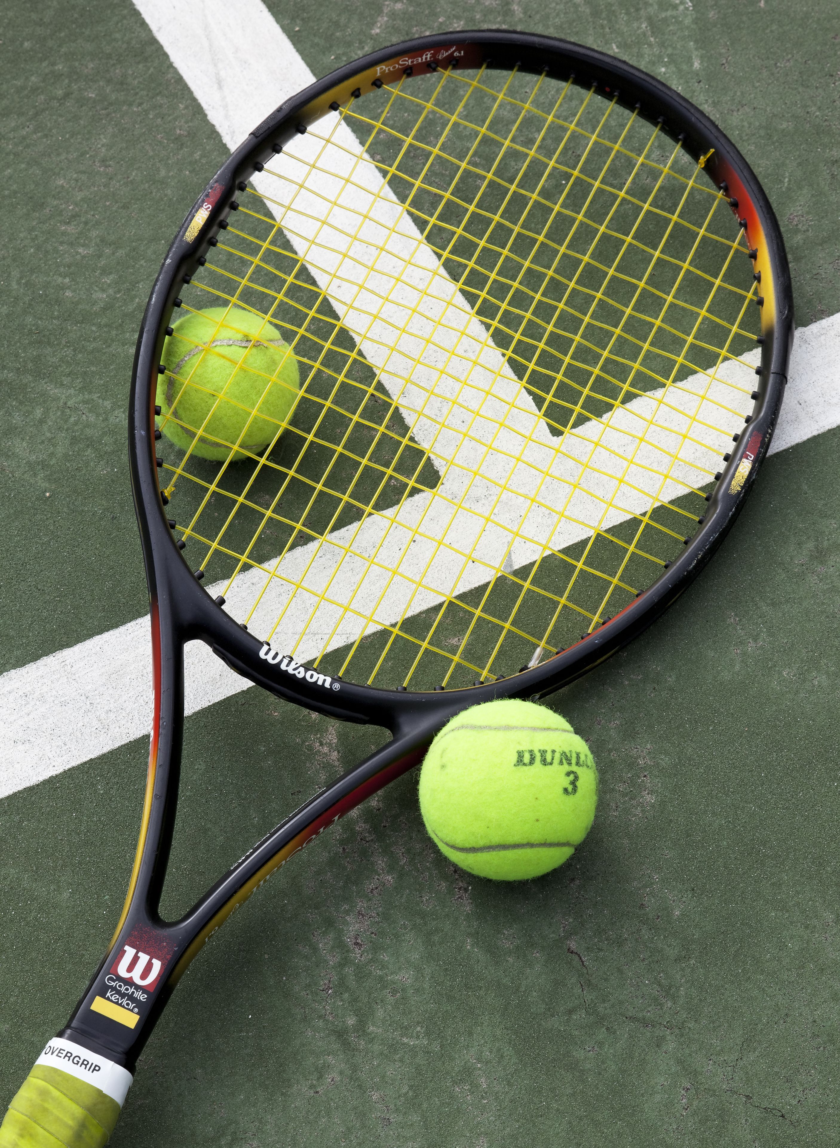 Una raqueta de tenis con empuñadura amarilla y una pelota de tenis en una cancha verde.