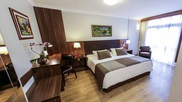 Habitación de hotel con una cama grande, un escritorio, una silla y dos cuadros en las paredes.
