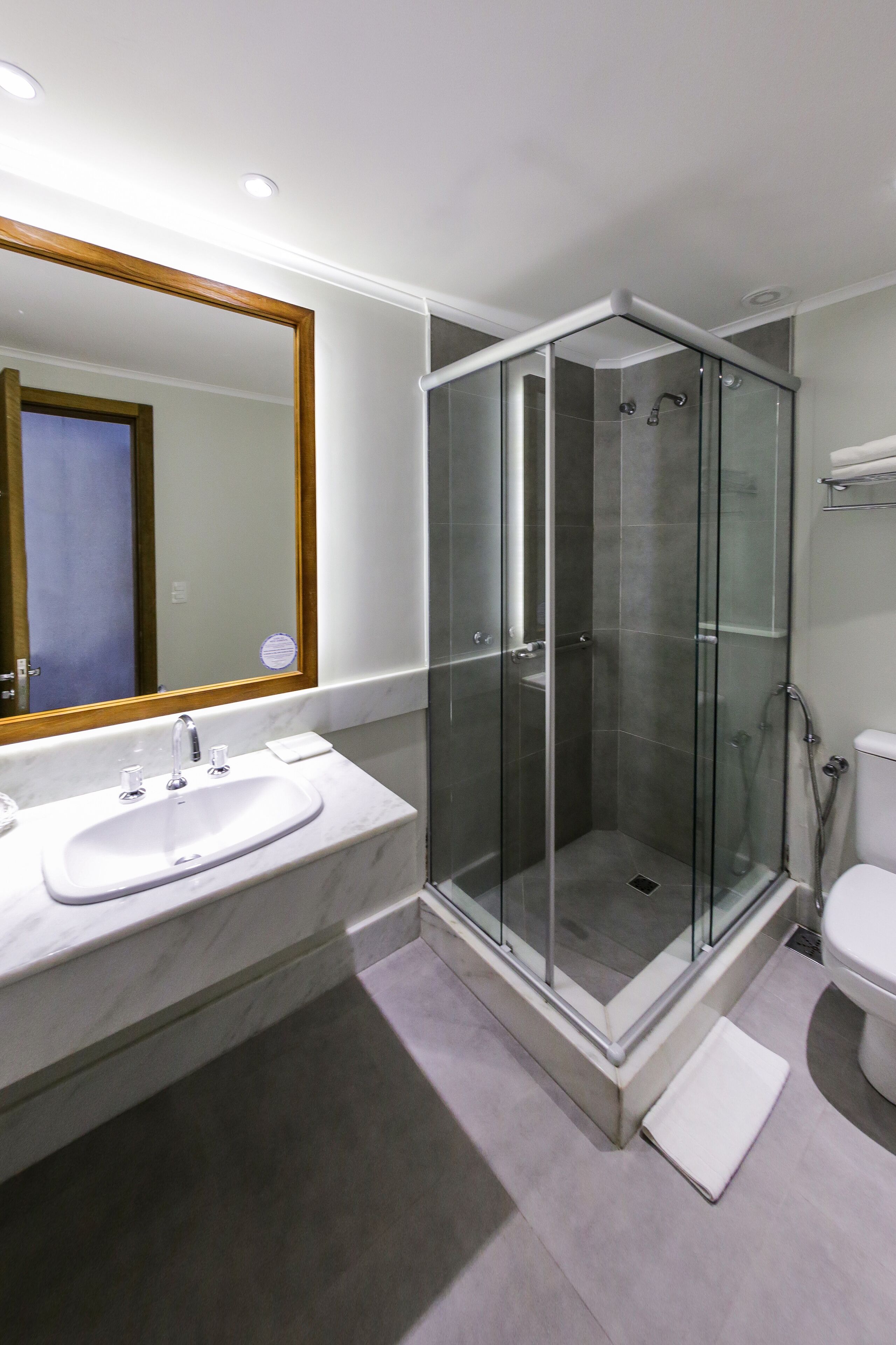 Un baño moderno con ducha envuelta en vidrio, un lavamanos blanco y un espejo grande.