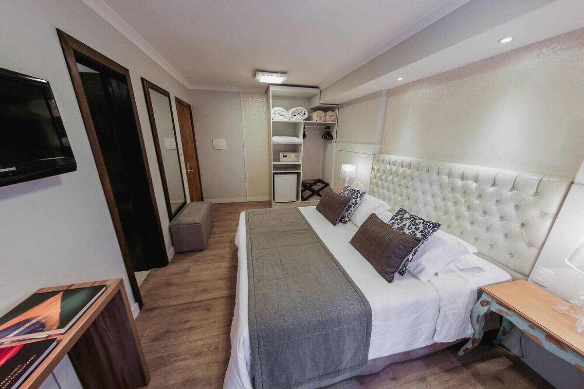 A hotel room with a bed, bedside table, TV, wardrobe, and a small kitchenette.