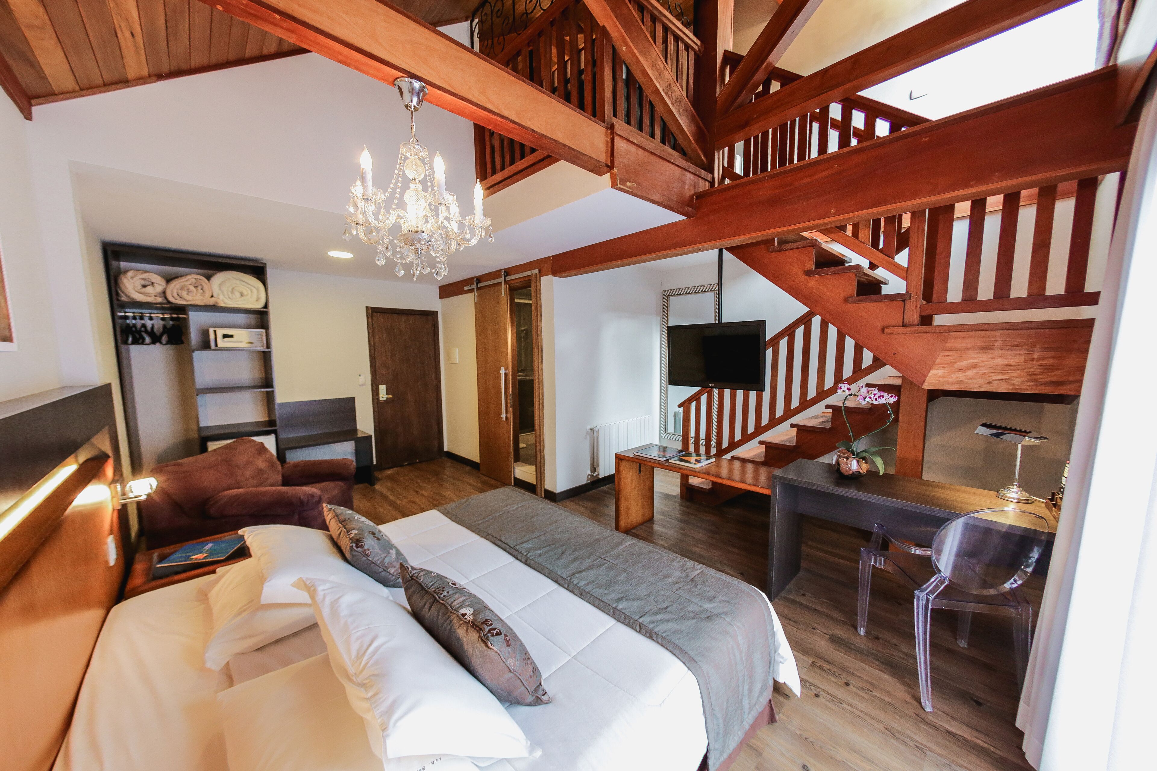 Een ruime slaapkamer met een groot bed, een houten trap, een bureau en een televisie.