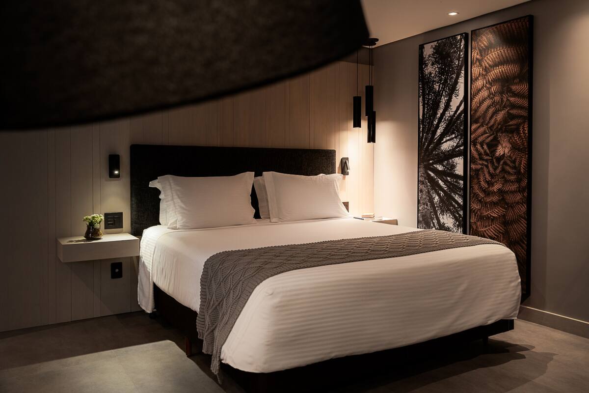 A modern bedroom with a large bed, bedside tables, and a wall-mounted artwork.