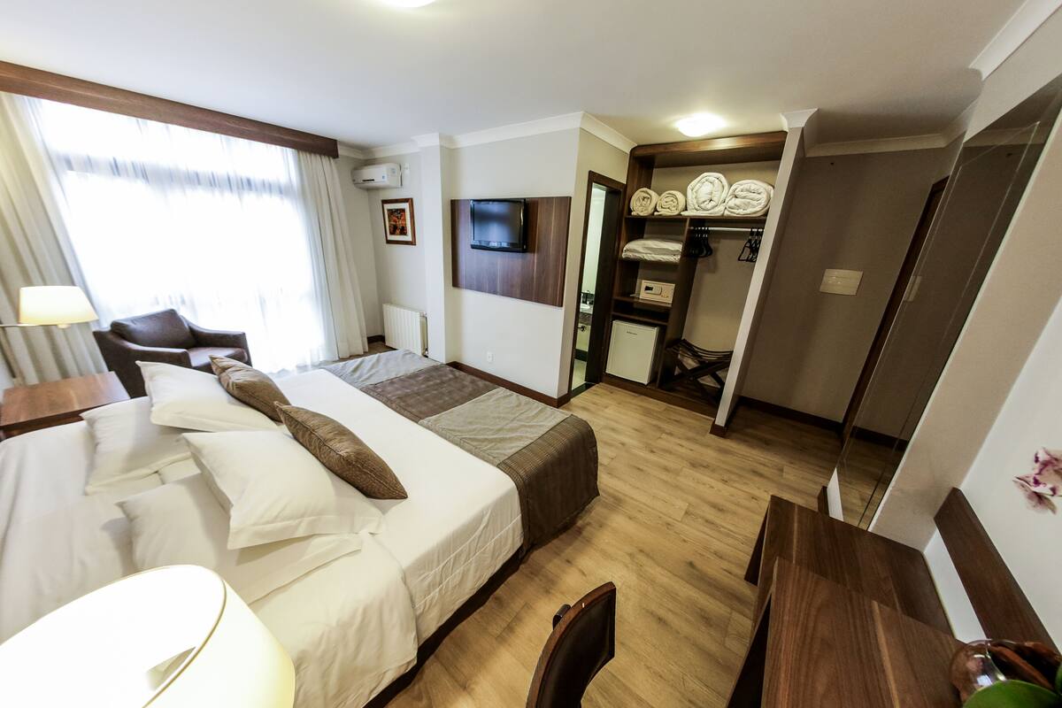 A hotel room with a bed, a desk, a chair, a TV, a wardrobe, and a bathroom.