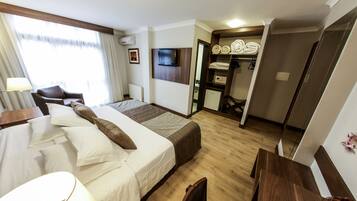 Quarto de hotel com cama, escrivaninha, cadeira, televisão, guarda-roupa e banheiro.