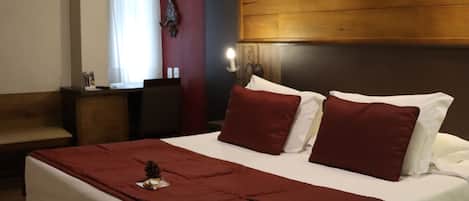 A hotel room with a large bed, a wooden headboard, a nightstand, and a wall-mounted clock.