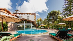 A pool area with lounge chairs and umbrellas, surrounded by a wooden deck and greenery. - Bavaria Sport Hotel (Gramado)