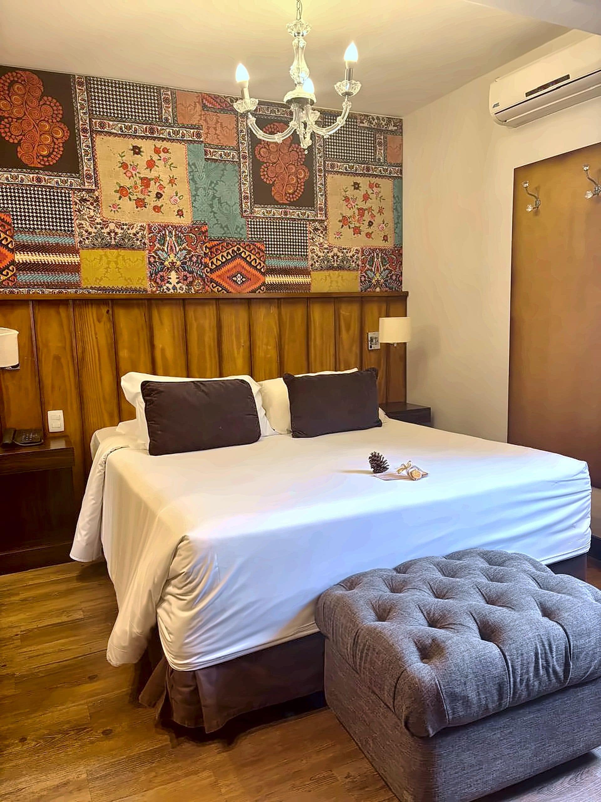 Una habitación de hotel con una cama grande, una araña, un tapiz de pared estampado y un cabecero de madera.