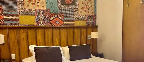 Una habitación de hotel con una cama grande, una araña, un tapiz de pared estampado y un cabecero de madera.