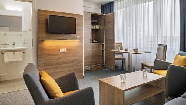 A modern hotel room with a wooden wall, a flat-screen TV, a dining area, and a sofa. - Gästehaus Lütten Klein (Rostock)