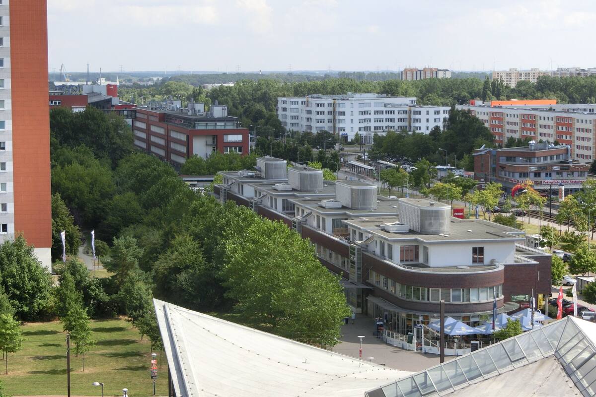 Un edificio moderno con múltiples unidades de aire acondicionado en el techo, rodeado de vegetación y otros edificios.