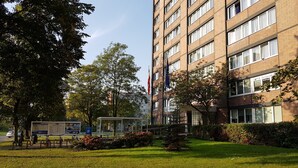 A multi-story building with a brick facade, large windows, and a well-maintained lawn with trees and shrubs. - Gästehaus Lütten Klein (Rostock)