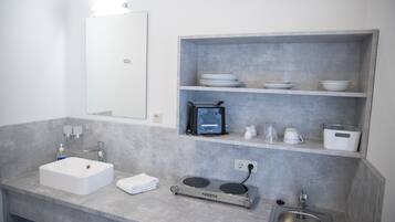 Uma casa de banho moderna com uma sanita branca, um espelho, um porta-toalhas, uma máquina de café e uma estante com pratos e chávenas.