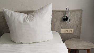 A neatly made bed with a pillow, a small round table, and a wall-mounted light fixture.