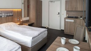 A hotel room with a bed, bedside table, lamp, and a small kitchenette area with a microwave and a coffee maker. - Gästehaus Lütten Klein (Rostock)
