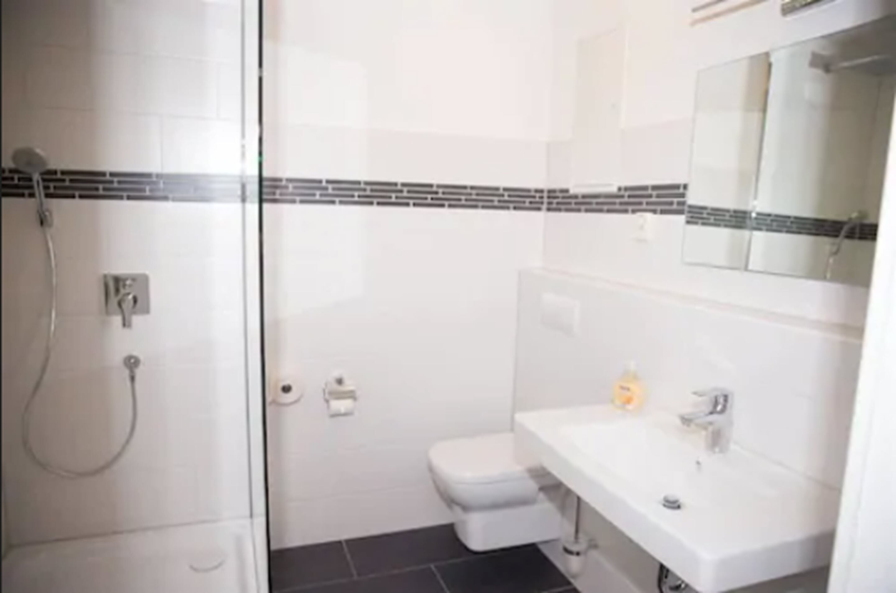 Casa de banho moderna com cabine de chuveiro de vidro, lavatório branco e sanita.