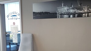 A waiting area with a chair, a small table, a potted plant, and a wall-mounted picture of a ship. - Gästehaus Lütten Klein (Rostock)