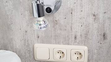 A bathroom with a shower head mounted on a textured wall, a white sink, and a power outlet with three sockets.