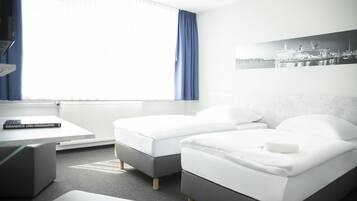 Habitación de hotel con dos camas, un escritorio y una ventana con cortinas.