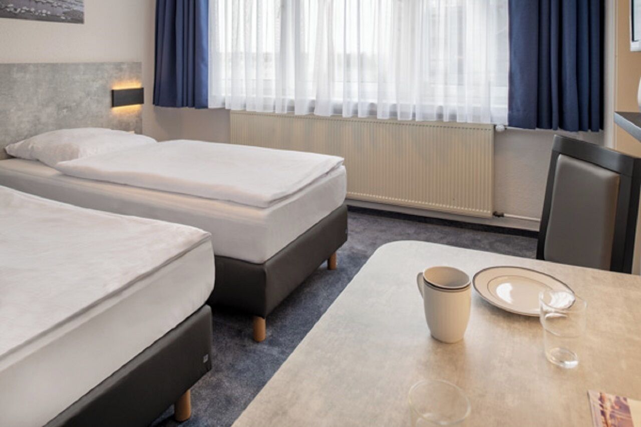 Ein Hotelzimmer mit zwei Betten, einem Tisch mit Teller und Tasse sowie einem Fenster mit Vorhängen.