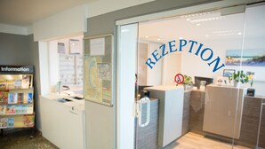A reception area with a glass door, a reception desk, and a wall-mounted information board. - Gästehaus Lütten Klein (Rostock)