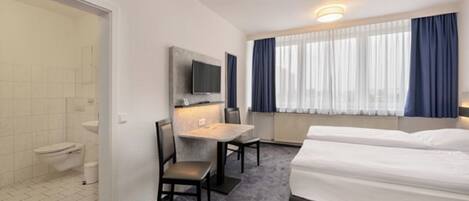 A hotel room with a bed, a desk, a chair, a TV, and a window with curtains.
