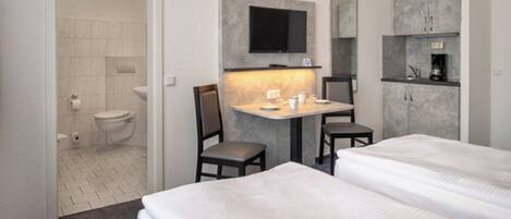 A hotel room with a bed, a desk with two chairs, a television, and a small kitchenette.