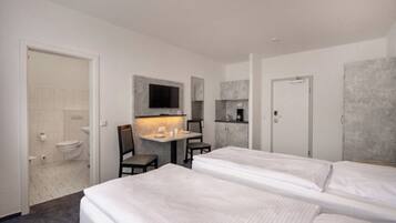Ein Hotelzimmer mit zwei Betten, einem kleinen Schreibtisch mit Stuhl, einem an der Wand befestigten Fernseher und einem Badezimmer mit Toilette und Waschbecken.