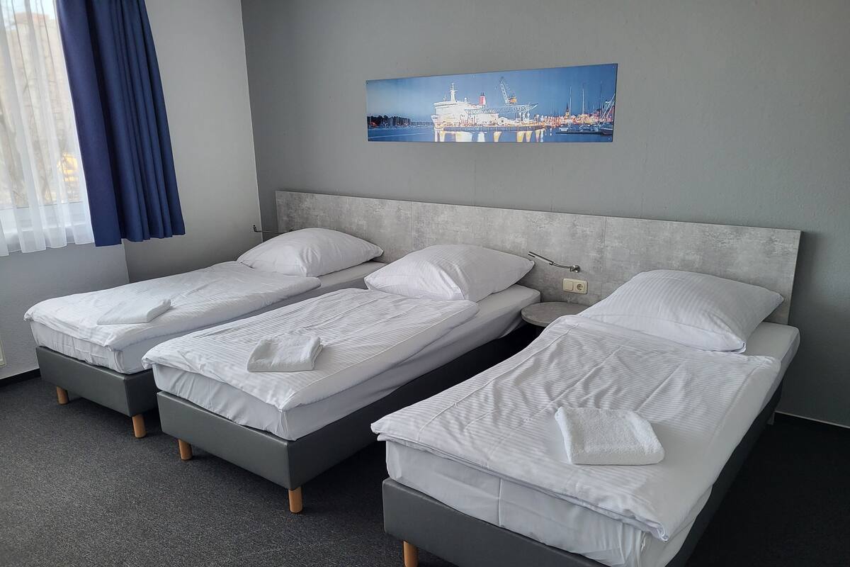 Una habitación de hotel con dos camas individuales, un cabecero gris, una mesita redonda y un cuadro en la pared.