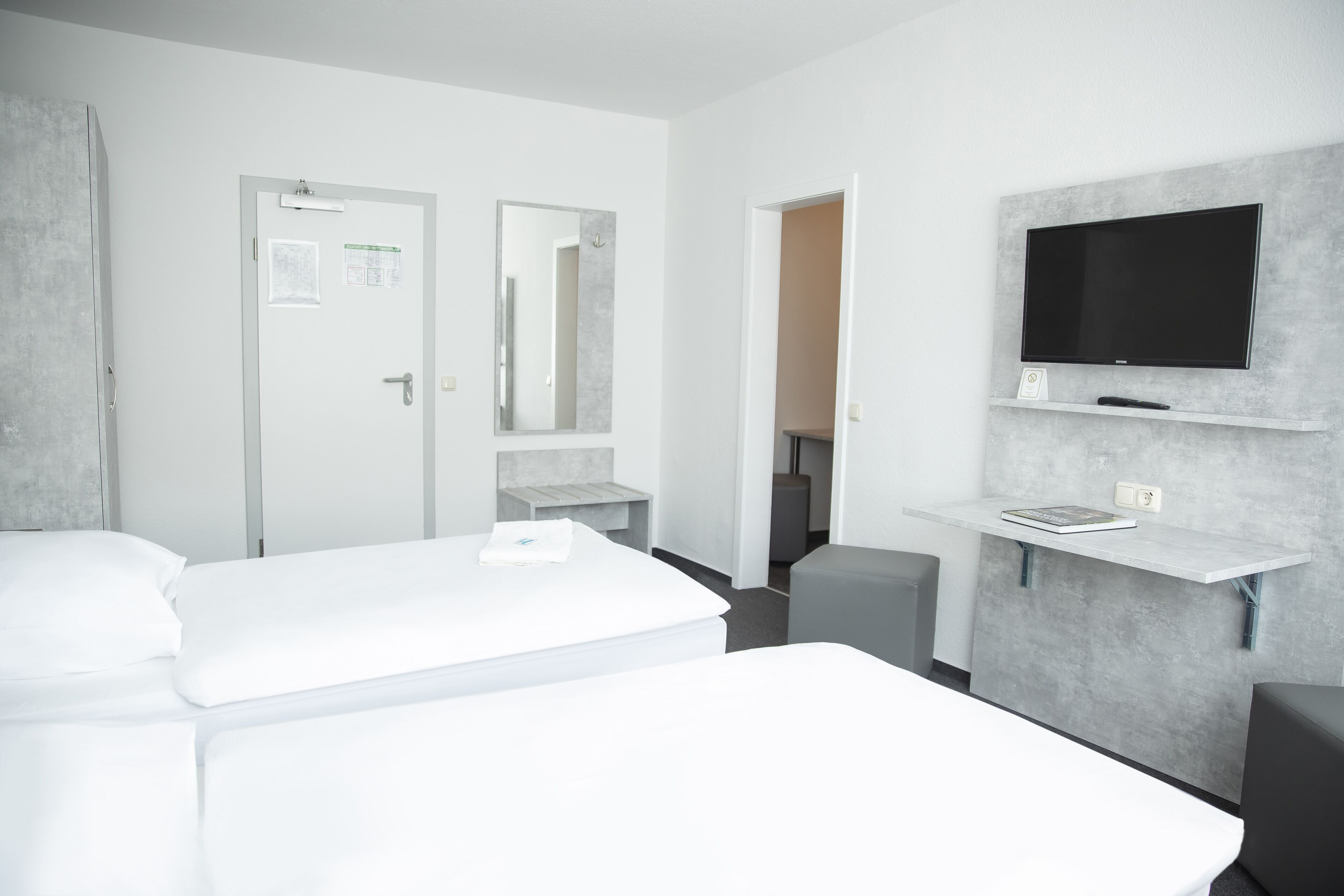 Une chambre d’hôtel moderne avec un grand lit, un téléviseur fixé au mur et un petit bureau avec une chaise.