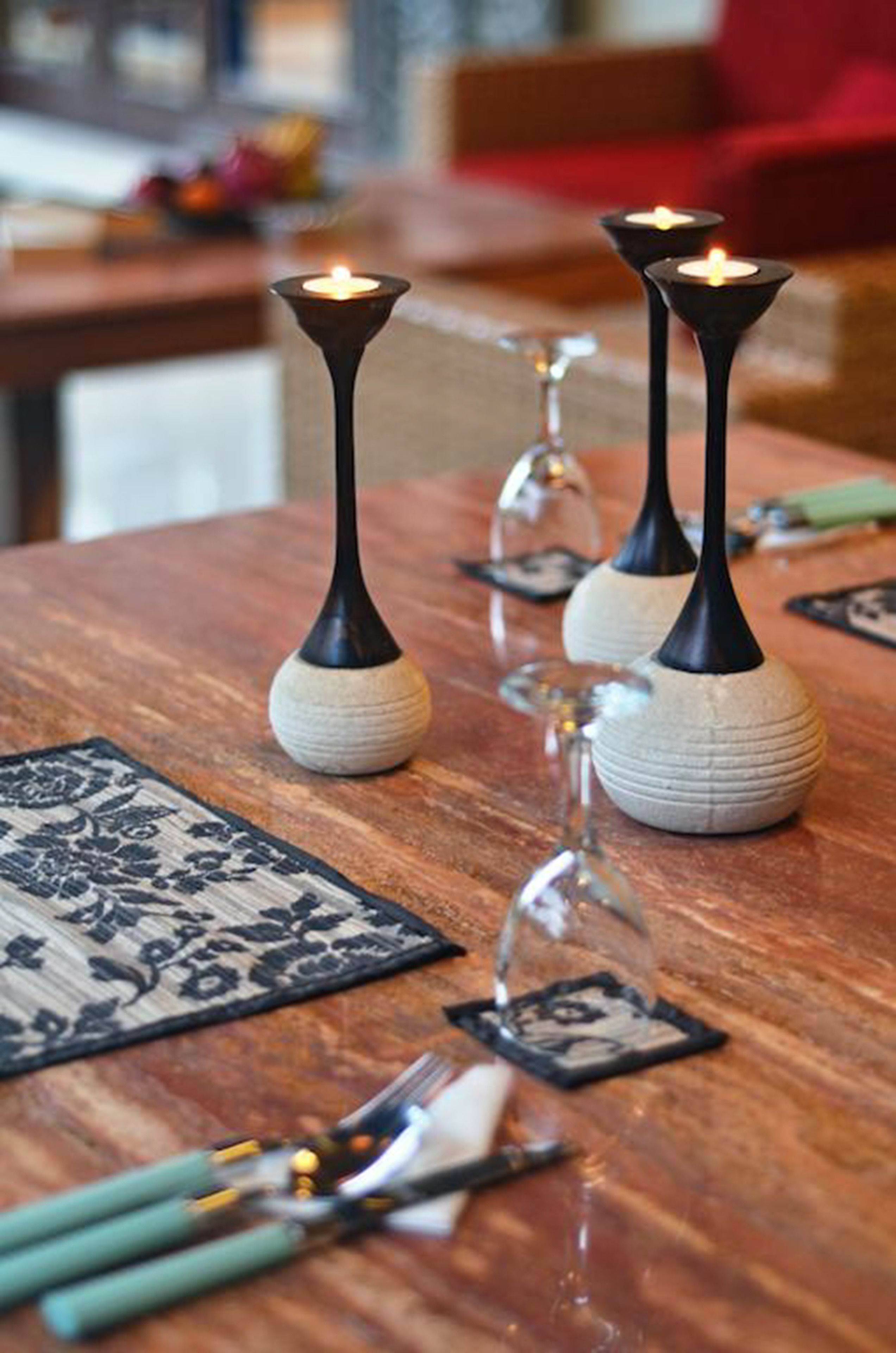 A wooden table with three black candle holders, a glass vase, and a patterned placemat.