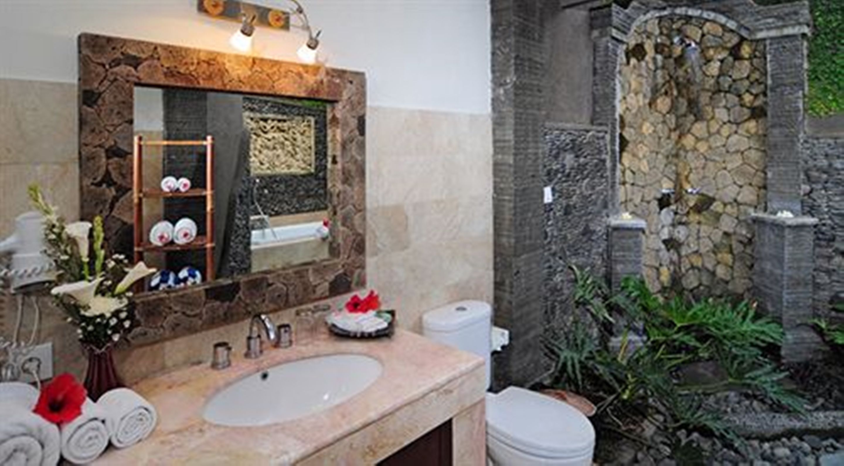 Une salle de bain avec un lavabo en pierre, un miroir, un porte-serviettes et un espace douche doté d’un mur en pierre.